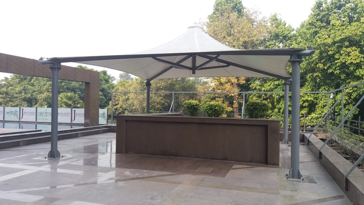 Img20190703wa0027 archilexis | premium tensile structure manufacturer Outdoor Terrace with a White Canopy Shelter over a Dark Brown Counter Set on a Tiled Floor with Glass Railing and Green Trees in the Background