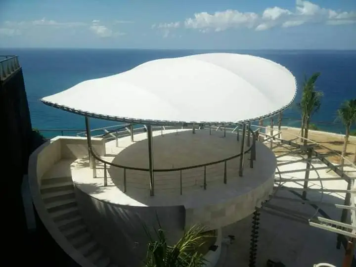 Circular Coastal Viewing Deck with a White Sail like Canopy Open to the Sea and Sky Metal Rails and Stairs Along the Left Side