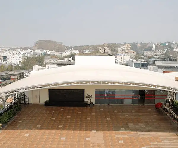 Images 1 archilexis | premium tensile structure manufacturer Rooftop Terrace with a White Curved Canopy over a Tiled Courtyard City Buildings Visible in the Distance